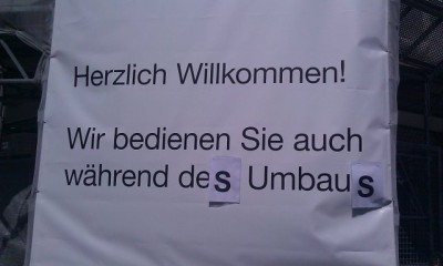 Korrgierter Text auf überdimensionaler Werbeplane: "Wir bedienen Sie auch während dem (des) Umbau (Umbaus)" DIN A3 Papier auf Plane, Kreuzplatz, Zürich